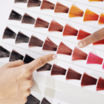 Two hands pointing to hair color swatches on a chart in a Palm Beach County salon, illustrating the variety of options available for a hair coloring service.