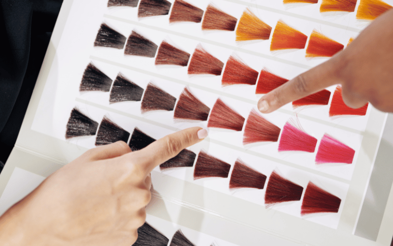 Two hands pointing to hair color swatches on a chart in a Palm Beach County salon, illustrating the variety of options available for a hair coloring service.