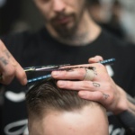 A close-up of a stylist at Theaology Salon & Day Spa in Florida, skillfully cutting a man's hair with scissors and a comb.