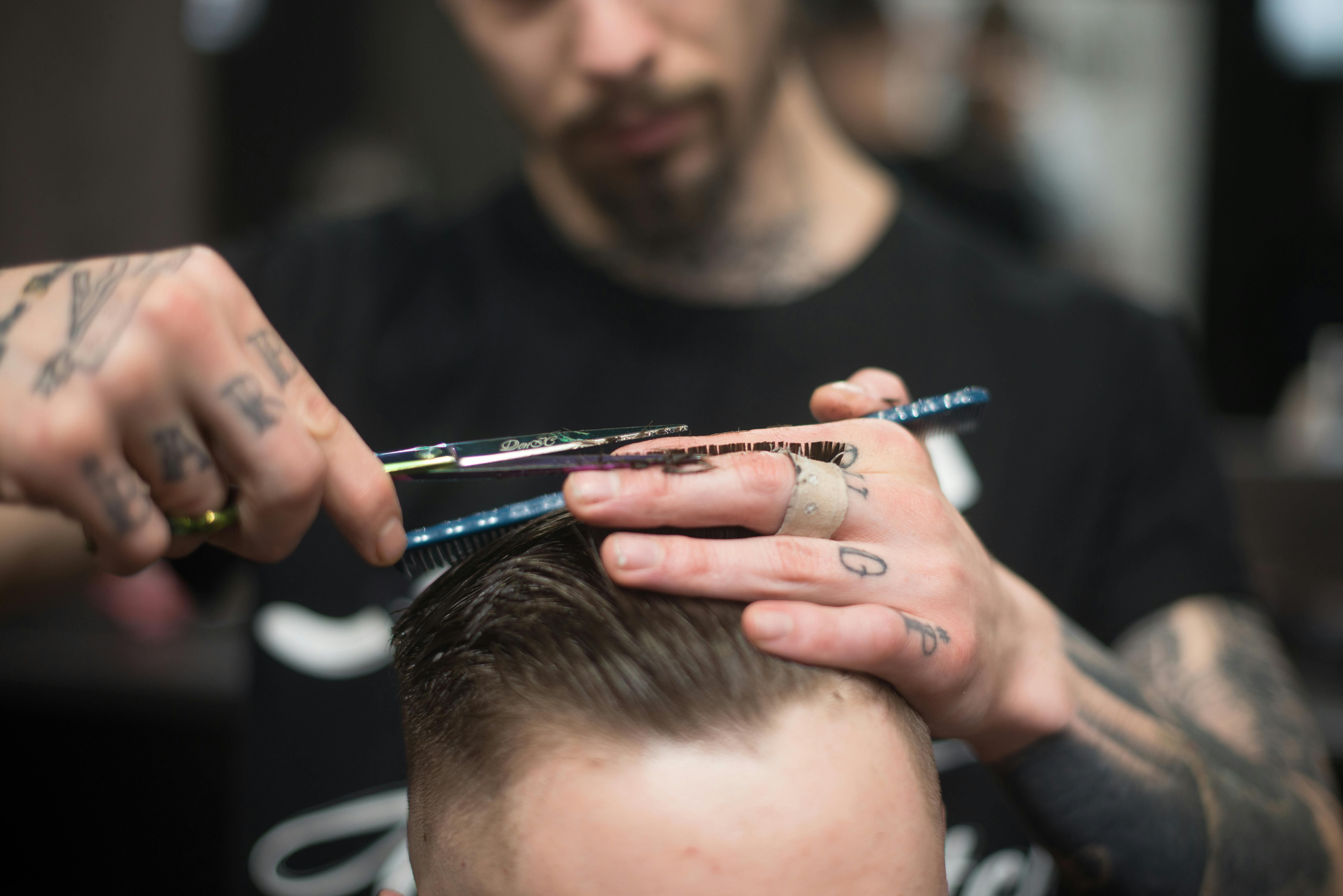 A close-up of a stylist at Theaology Salon & Day Spa in Florida, skillfully cutting a man's hair with scissors and a comb.