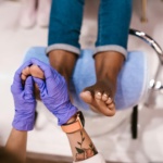 A close-up of a person receiving a professional pedicure in Palm Beach Gardens, with a focus on the foot massage being performed by a specialist wearing purple gloves.