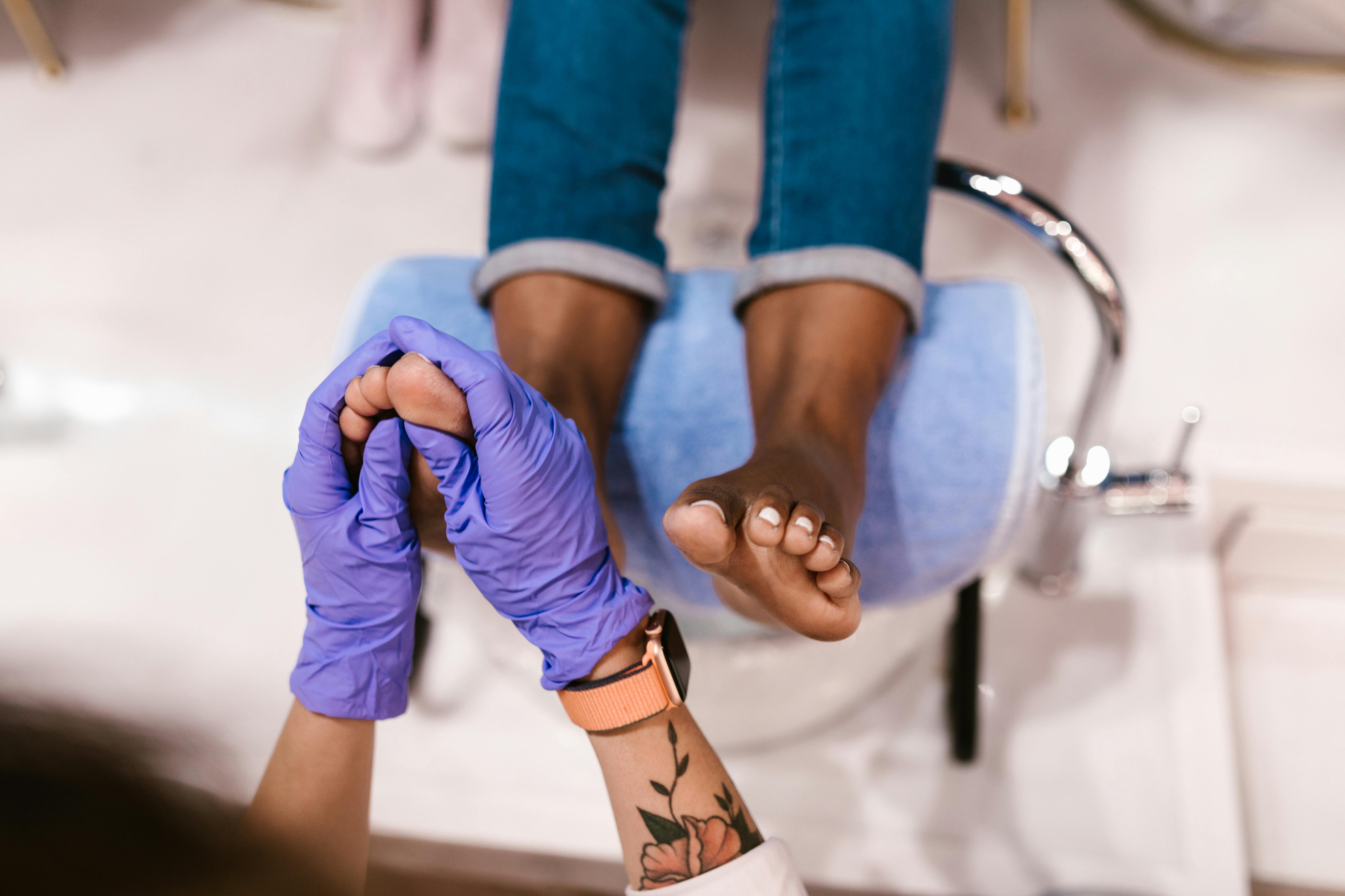 A close-up of a person receiving a professional pedicure in Palm Beach Gardens, with a focus on the foot massage being performed by a specialist wearing purple gloves.