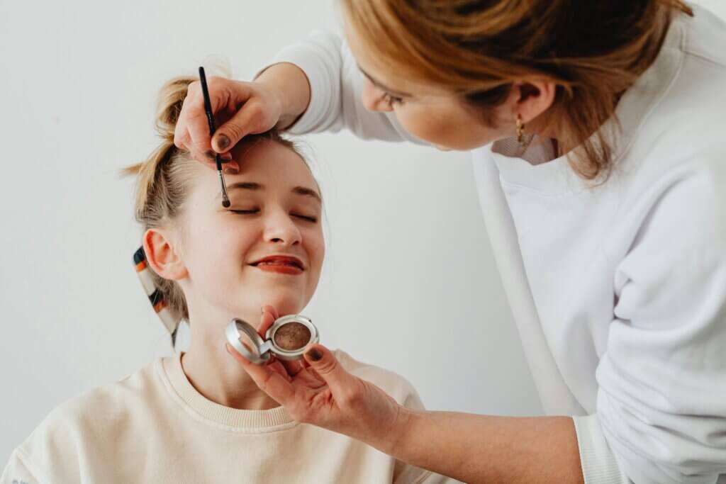 Professional makeup artist in Palm Beach applying eyeshadow to a smiling client, showcasing expertise in creating different makeup styles for all occasions.