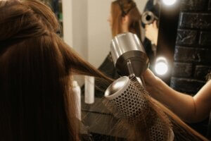 A hairstylist using a round brush and blow dryer to style a client’s hair in a salon, ensuring a smooth treatment for hair with a sleek, polished finish.