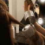 A stylist using a round brush and hair dryer to smooth a client’s hair during a salon blowout at a professional hair salon.