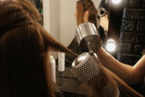 A stylist using a round brush and hair dryer to smooth a client’s hair during a salon blowout at a professional hair salon.