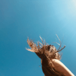 Woman’s hair blowing in the wind under a bright sky, showcasing the importance of easy hairstyles for humid weather