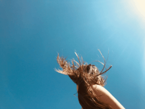 Woman’s hair blowing in the wind under a bright sky, showcasing the importance of easy hairstyles for humid weather