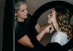 A makeup artist applies makeup to a client's face using a brush, illuminated by a ring light. The artist focuses intently while the client, seated and wearing a robe, remains still. The setting appears to be a professional studio, highlighting the expertise and attention to detail in the makeup application process. This image relates to choosing the right makeup artist in Palm Beach.