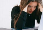 Woman looking stressed while working on a laptop, showing how stress affects skin hair and nails during daily life and work pressure