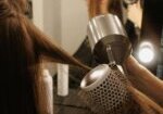 A stylist using a round brush and hair dryer to smooth a client’s hair during a salon blowout at a professional hair salon.