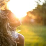 Golden sunlight shining through flowing blonde curls outdoors, highlighting potential UV damage to hair caused by prolonged sun exposure and dryness.