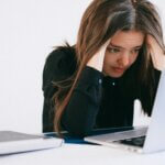 Woman looking stressed while working on a laptop, showing how stress affects skin hair and nails during daily life and work pressure