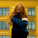 Woman with voluminous curly hair standing in front of a yellow building, showing natural curl movement before a keratin treatment for curly hair