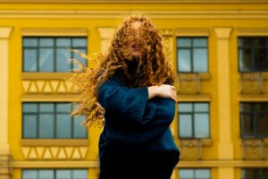 Woman with voluminous curly hair standing in front of a yellow building, showing natural curl movement before a keratin treatment for curly hair